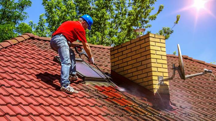 Professionelle Dachreinigung Rhein Main - Mitarbeiter reinigt rotes Ziegeldach mit Hochdruckreiniger für saubere Dachziegel