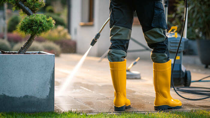 Pflasterreinigung Frankfurt - Bautenschutz Mitarbeiter reinigt Steinboden mit Hochdruckreiniger in Gummistiefeln